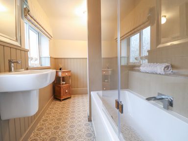 A bathroom with a bathtub sink wooden cabinet and patterned floor at 3 Ivy Court in Dolgellau