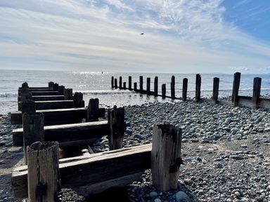 A pebble beach with old wooden groynes extending into the sea under a partly cloudy sky at Deu-Ddrws in Barmouth