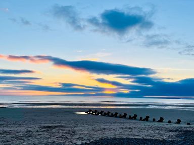 A beach with wooden groynes and a sunset over the sea at Deu-Ddrws in Barmouth