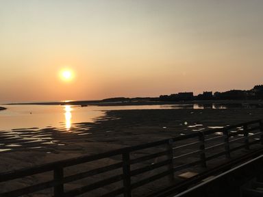 A sunset over a body of water with a sandy shore and buildings in the distance at Deu-Ddrws in Barmouth