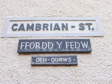 Three street signs on a wall showing Cambrian St Ffordd Y Fedw and Deu-Ddrws in Barmouth