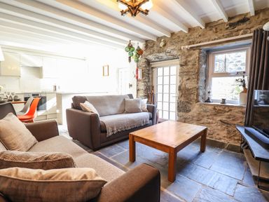 A living room with two sofas a wooden coffee table stone walls and a kitchen area with orange chairs at Deu-Ddrws in Barmouth