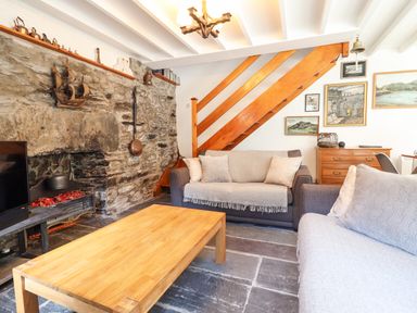 A living room with two sofas a wooden coffee table a stone fireplace and wooden staircase at Deu-Ddrws in Barmouth