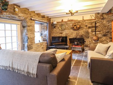 A sitting room with stone walls a television a fireplace two sofas and a wooden table at Deu-Ddrws in Barmouth