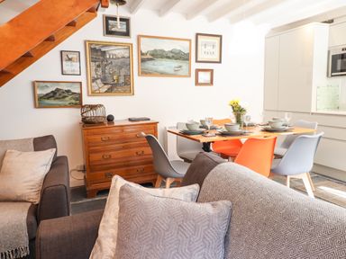 A dining area with a wooden table set for six people chairs a wooden chest of drawers paintings on the wall and part of a sofa in Deu-Ddrws Barmouth