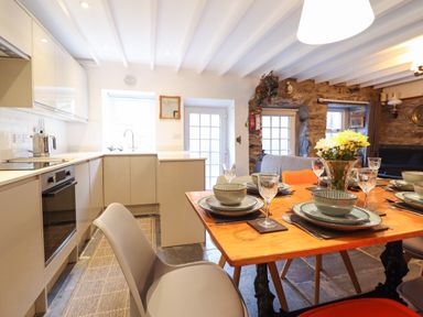 A kitchen and dining area with dishes set on a wooden table and a stone wall in the background at Deu-Ddrws in Barmouth