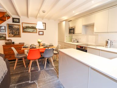 A kitchen and dining area with a dining table set with plates and flowers and a kitchen island at Deu-Ddrws in Barmouth