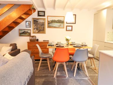 A dining area with a wooden table, six chairs, and a wooden dresser under a staircase at Deu-Ddrws in Barmouth