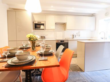 A kitchen with a dining table set for six and orange and beige chairs at Deu-Ddrws in Barmouth