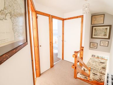 A hallway with three white doors framed in wood a staircase with wooden railing and framed maps on the walls at Deu-Ddrws in Barmouth