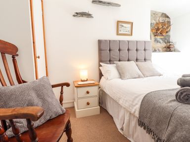 A bedroom with a bed a wooden chair a nightstand with a lamp and a ship model on the wall at Deu-Ddrws in Barmouth