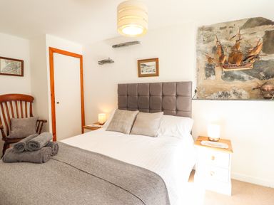 A bedroom with a bed gray pillows and blanket wooden chair bedside tables lamps and ship decoration on the wall at Deu-Ddrws in Barmouth
