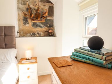 A bedroom corner with a bedside table lamp and books on a wooden surface near a window at Deu-Ddrws in Barmouth