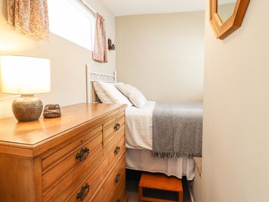 A bedroom with a single bed next to a wooden chest of drawers with a lamp on it at Deu-Ddrws in Barmouth