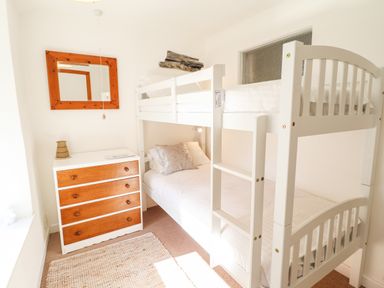 A bedroom with white bunk beds a wooden dresser with drawers and a wall mirror at Deu-Ddrws in Barmouth