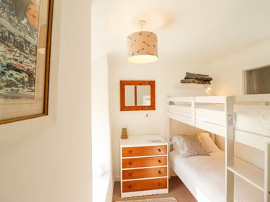 A small bedroom with a bunk bed a chest of drawers and a wall mirror at Deu-Ddrws in Barmouth