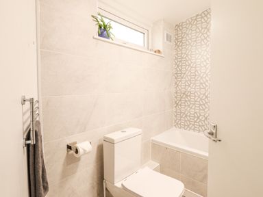 A bathroom with a toilet a towel hanging on a rack a bathtub and a small window with a plant on the ledge at Deu-Ddrws in Barmouth