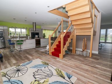 An open kitchen and dining area with a wooden staircase with red carpet and a patterned rug on the floor at Ty Marlyn in Crofty