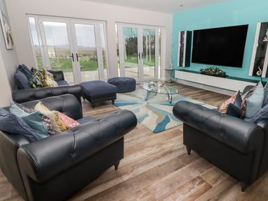 A living room with black leather sofas a glass coffee table large TV and glass doors at Ty Marlyn in Crofty