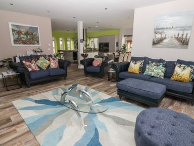 A living room with blue sofas and a glass coffee table with dolphin sculptures at Ty Marlyn in Crofty