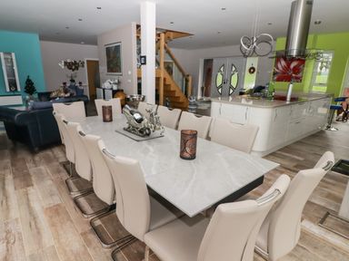 A dining room with a marble table and beige chairs next to a kitchen with a green wall and modern appliances at Ty Marlyn in Crofty