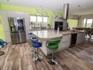 A kitchen with a large island and bar stools in blue and green at Ty Marlyn in Crofty