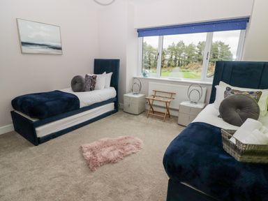 A bedroom with two single beds two nightstands a window with blue blinds and a small pink rug on the floor at Ty Marlyn in Crofty