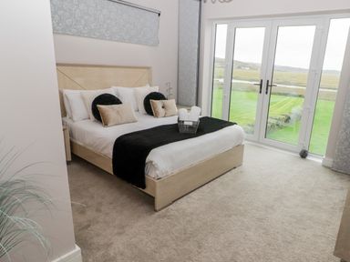 A bedroom with a bed cushions and a basket of towels near glass doors overlooking a lawn at Ty Marlyn in Crofty