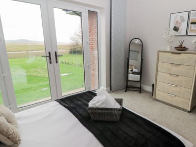 A bedroom with a bed near glass doors with a view of green grass a dresser a standing mirror and framed art at Ty Marlyn in Crofty