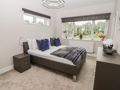A bedroom with a grey bed and blue pillows beside a window with trees outside at Ty Marlyn in Crofty