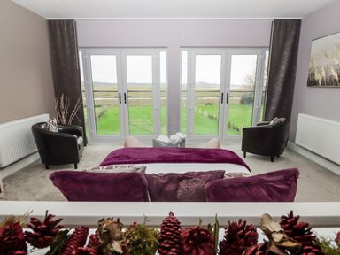 A living room with two black chairs and purple cushions facing glass doors overlooking a grassy area at Ty Marlyn in Crofty