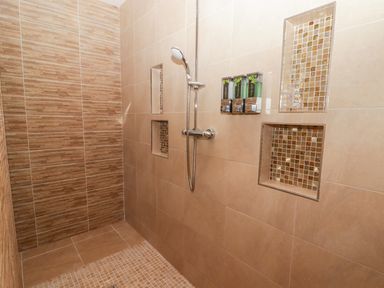 A tiled walk-in shower with built-in shelves and wall-mounted shampoo dispensers at Ty Marlyn in Crofty