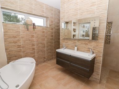 A bathroom with a double sink vanity a freestanding bathtub and a decorative vase on the window at Ty Marlyn in Crofty