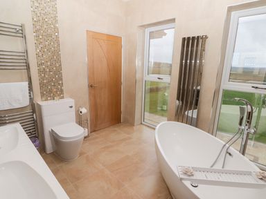 A bathroom with a freestanding bathtub a toilet a double sink and two windows at Ty Marlyn in Crofty