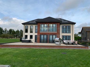 A modern two-story house with a brick and white exterior lawn and patio with outdoor furniture and a grill at Ty Marlyn in Crofty