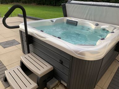 An outdoor hot tub with water and steps on a tiled patio near grass at Ty Marlyn in Crofty