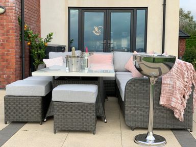 An outdoor seating area with a wicker sofa and stools around a white table with champagne bottles at Ty Marlyn in Crofty
