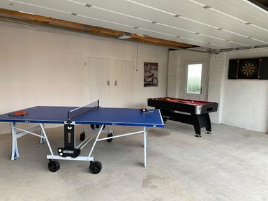 A recreational room with a blue table tennis table and a black pool table with a dartboard on the wall at Ty Marlyn in Crofty