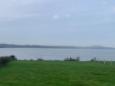 A grassy field bordered by fences leading to a body of water with hills in the background at Ty Marlyn in Crofty