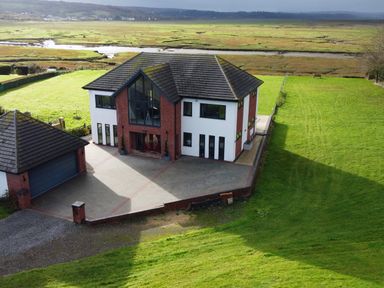 A modern two-story house with a garage and driveway surrounded by green fields at Ty Marlyn in Crofty