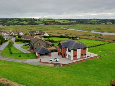 A house with a driveway and a car surrounded by green fields and other houses in the background at Ty Marlyn in Crofty