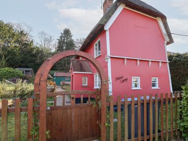 A red cottage with white trim behind a wooden fence and gate at Rhubarb Cottage in Ufford near Woodbridge