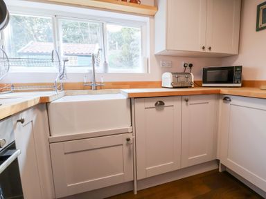 A kitchen with a sink a toaster a microwave and cabinets at Rhubarb Cottage in Ufford near Woodbridge