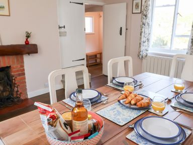 A dining table set with plates forks glasses of orange juice and a plate of croissants in a room with a fireplace at Rhubarb Cottage in Ufford near Woodbridge