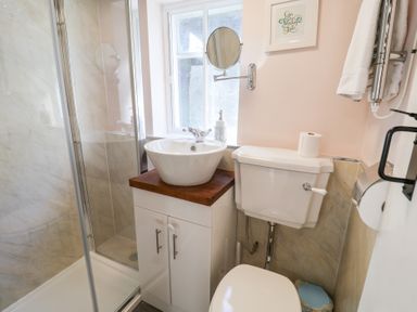 A bathroom with a shower enclosure sink with wooden countertop toilet and a window at Rhubarb Cottage in Ufford near Woodbridge