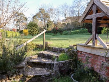 A garden with stone steps and a wooden well structure at Rhubarb Cottage in Ufford near Woodbridge