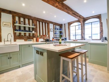 A kitchen with wooden beams green cabinets an island with two stools and large windows at The Bridewell in Woodbridge