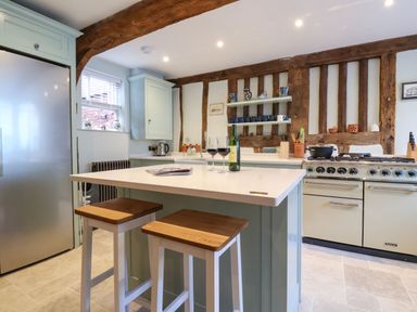 A kitchen with wooden beams a stove an island with two stools and a refrigerator at The Bridewell in Woodbridge