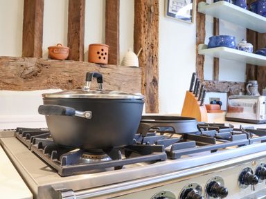 A kitchen stove with pots and knives with wooden beams and shelves in the background at The Bridewell in Woodbridge