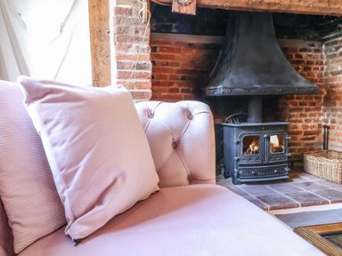 A pink sofa with cushions near a black wood burning stove in a brick fireplace at The Bridewell in Woodbridge